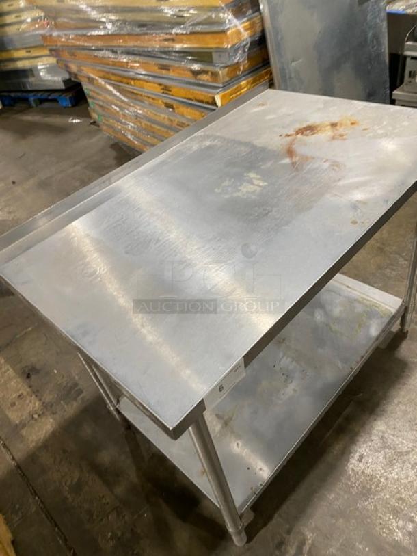 Stainless steel utility table with two shelves, signs of wear, surface rust, and scratches. Used condition, label with number 6.
