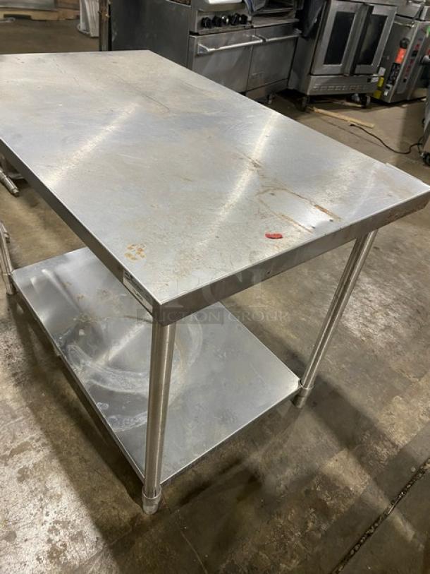 Stainless steel prep table with two shelves, mildly scratched surface. Sturdy legs, ideal for commercial kitchen use.
