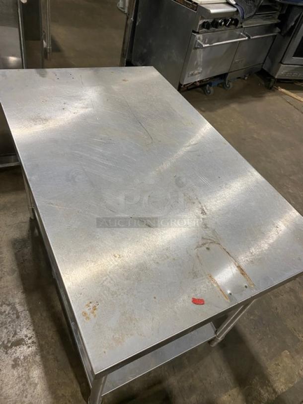 Stainless steel work table with visible scratches and slight rust marks, durable construction, suitable for industrial kitchens.