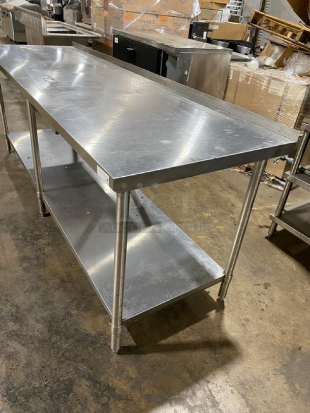 Stainless steel commercial work table with lower shelf, used condition. Smooth top surface, sturdy legs, ideal for kitchen use.