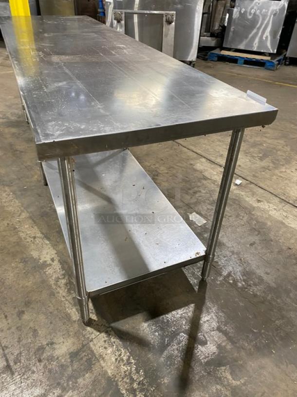 Stainless steel work table with lower shelf, slight surface scratches, sturdy construction, for industrial or kitchen use.