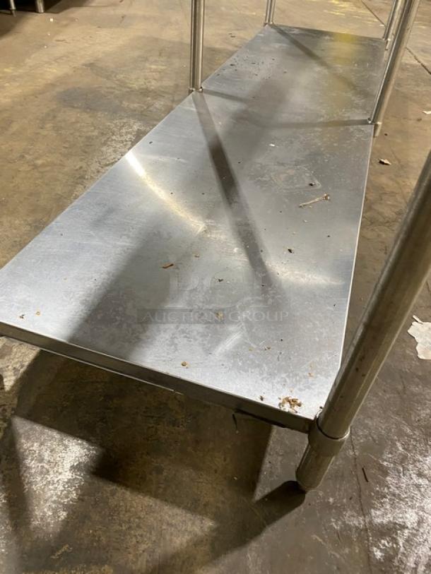 Metal storage shelf unit, dual-tiered, stainless steel, with visible wear and surface marks. Industrial use, sturdy construction.