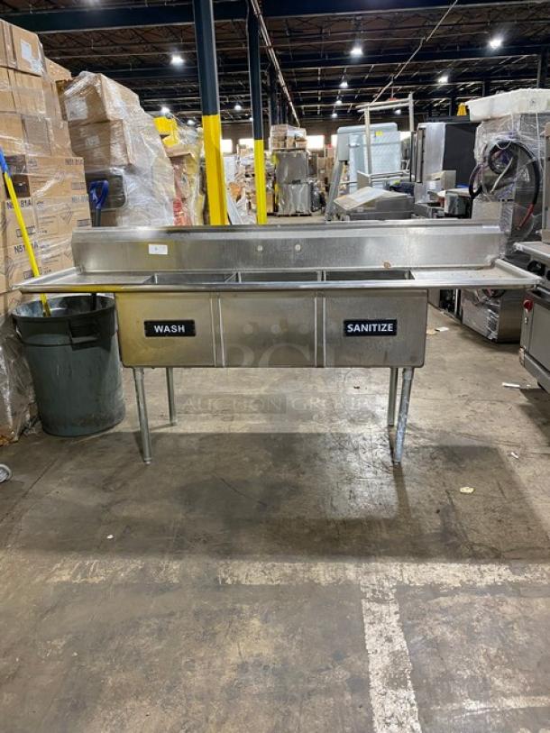 Stainless steel commercial sink with dual basins labeled "Wash" and "Sanitize," featuring drainboard, in used condition.