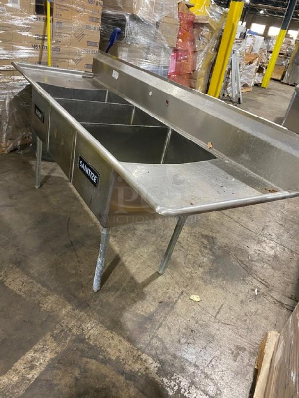 Stainless steel three-compartment sink with drainboards, labeled "Sanitize," commercial use, in good condition.