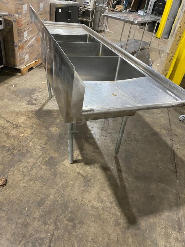 Stainless steel commercial triple sink, used, with sturdy legs and side splash guards, ideal for restaurant kitchens.