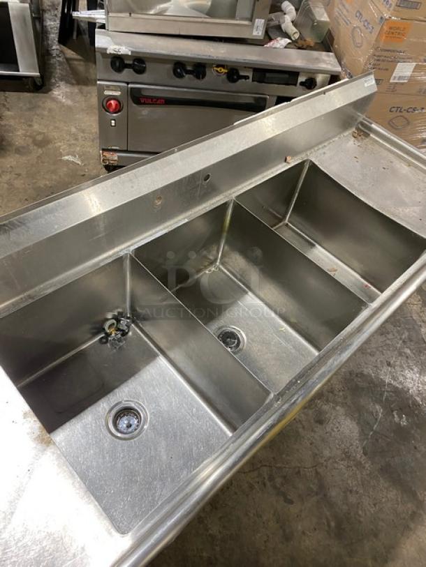 Stainless steel triple sink with drainboards, in used condition. Ideal for commercial kitchen use.