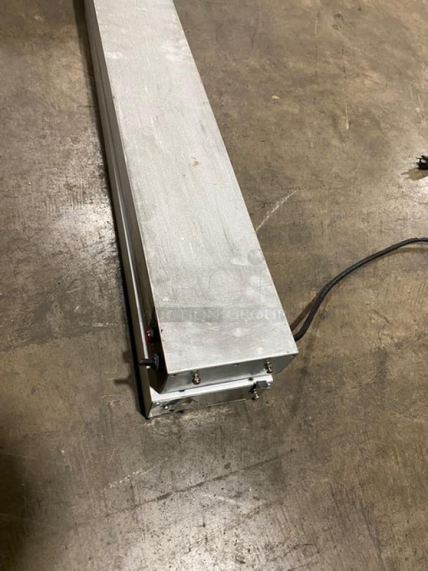 Metallic industrial light fixture with attached power cable, rectangular shape, showing some wear. Suitable for warehouse use.