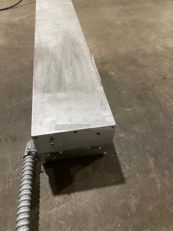 Metallic industrial fixture with a corrugated cable attachment, in used condition, on concrete flooring.