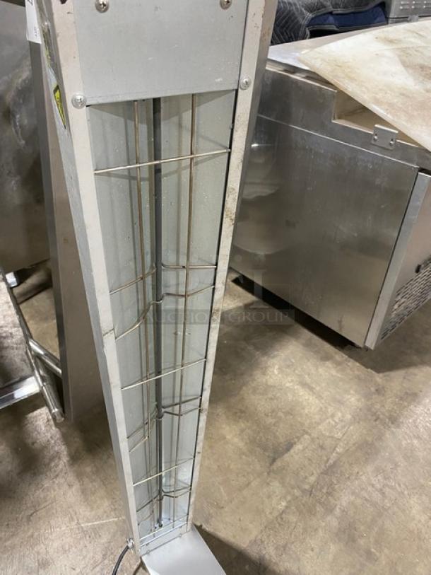 Industrial stainless steel heat lamp with protective wire guard. Signs of use visible. Ideal for commercial kitchens.