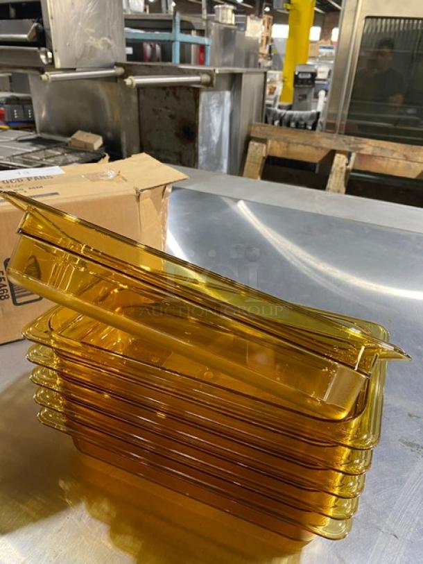 Stack of amber plastic food pans, likely new, nested on a stainless steel surface. Cardboard box in the background.