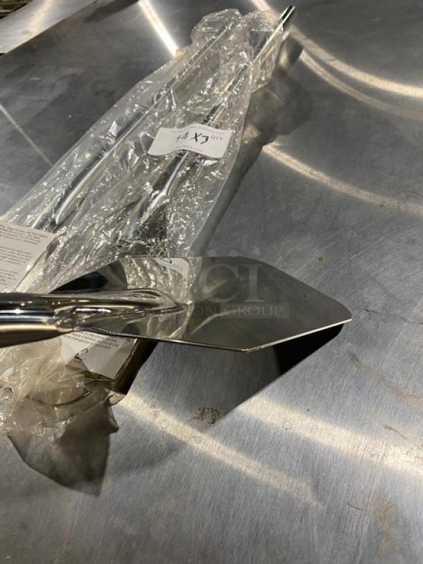 Stainless steel cake server, new, with protective plastic wrap. Features a serrated edge and shiny finish.