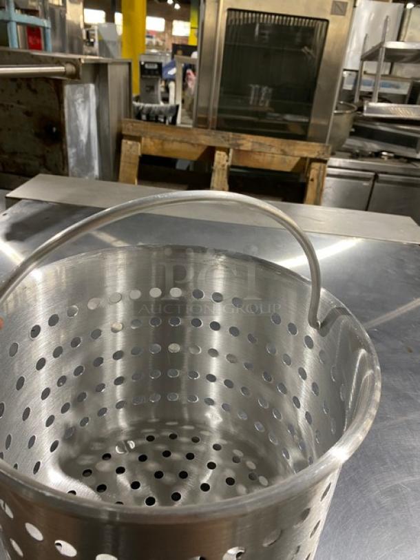 Stainless steel perforated basket with handle, kitchenware, excellent condition, industrial setting in background.