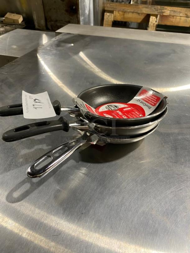 Set of three frying pans with non-stick coating, various sizes, black handles. Labels indicate new condition, ready for use.