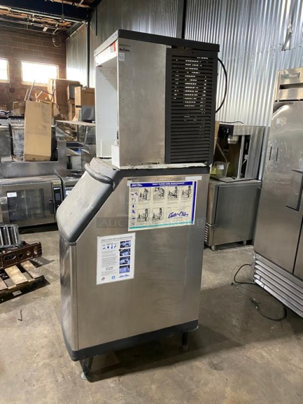 Commercial ice machine, metal exterior, model with top vent. Visible stickers with instructions and a brand logo. Good condition.