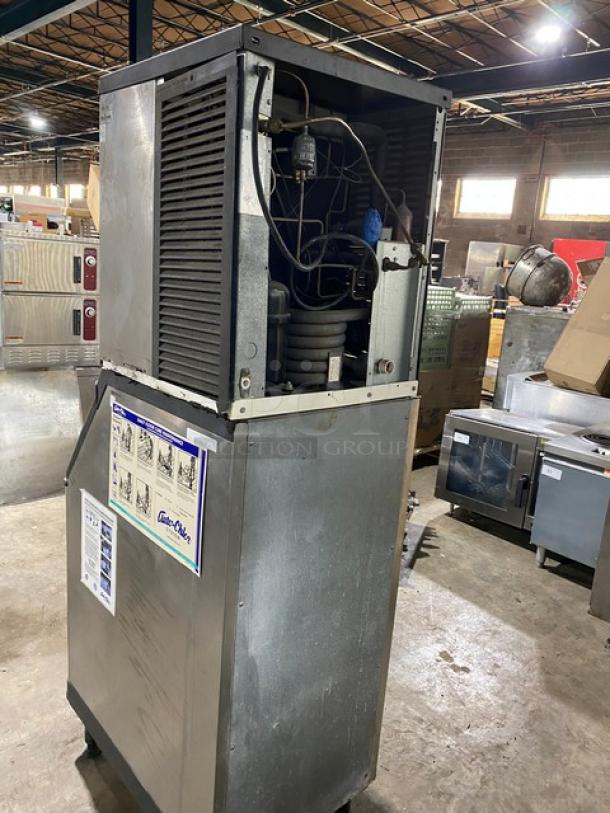 Industrial ice machine in worn condition, open panel showing internal components. Includes diagrams and operating instructions on panel.