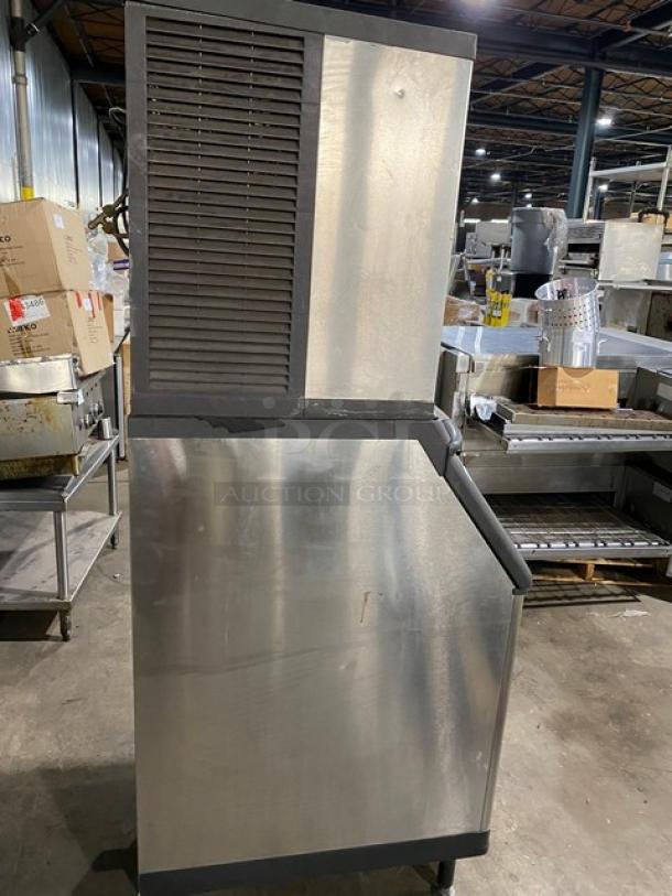 Commercial stainless steel ice maker in a warehouse setting. Features ventilation grille. Pre-owned, some surface wear.