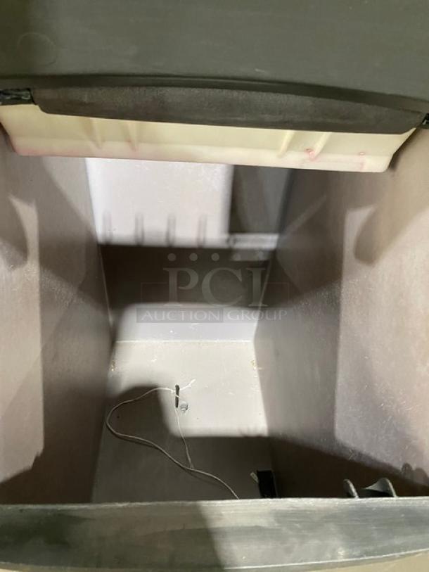 Open industrial ice maker interior, showing a spacious bin with slight dust and wire component. No visible labels or markings.