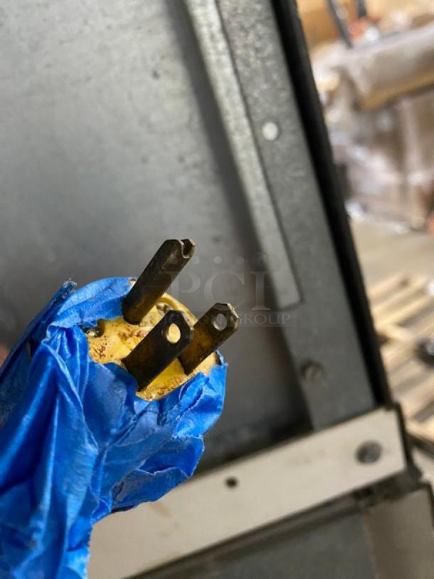 Yellow power plug with three prongs, partially covered in blue tape, showing signs of use. No visible labels or markings.