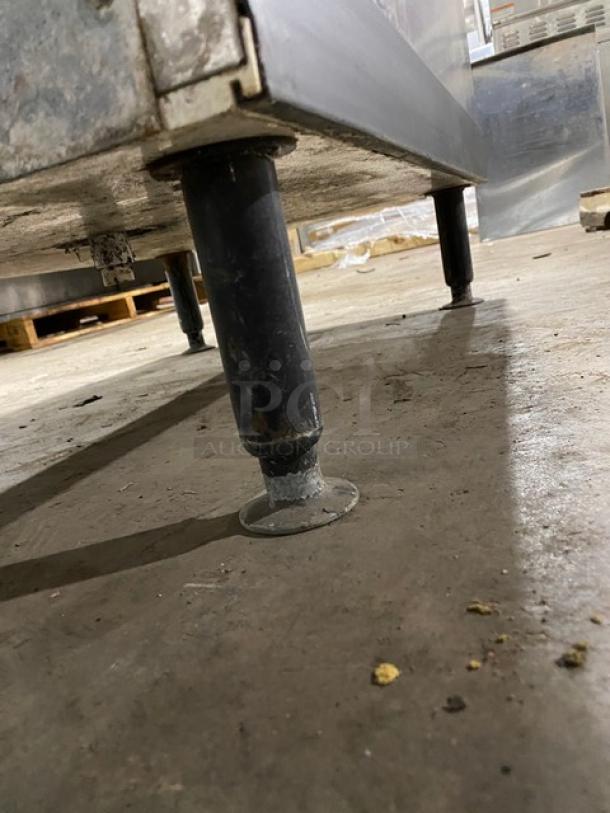 Stainless steel industrial table with adjustable legs, showing signs of wear. Ideal for commercial kitchen use.