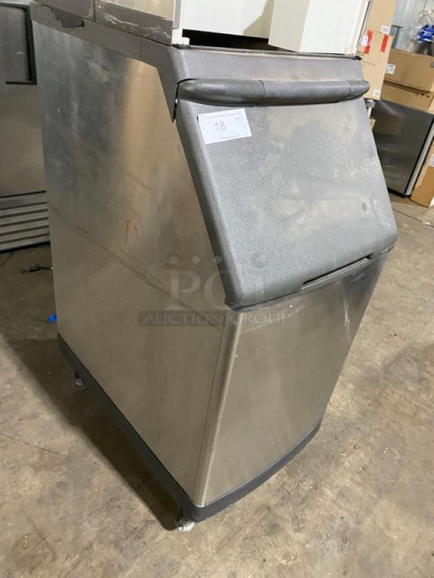 Stainless steel commercial ice maker, used condition, black top lid, visible label with number "18," on raised feet.