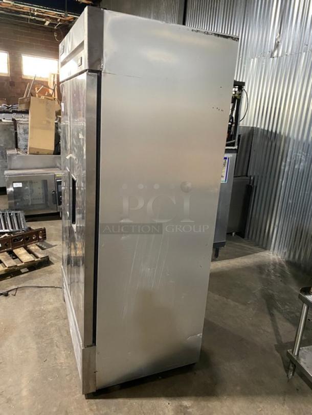 Stainless steel commercial refrigerator, single door, visible surface scratches, industrial setting.
