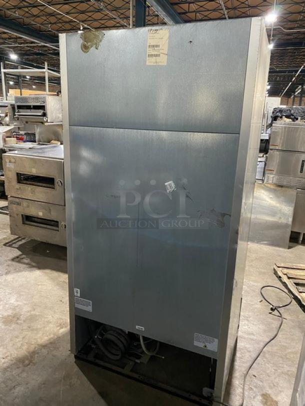 Commercial stainless steel refrigerator, used condition, visible scratches and dents, warehouse setting. Tags with wear, no legible markings.