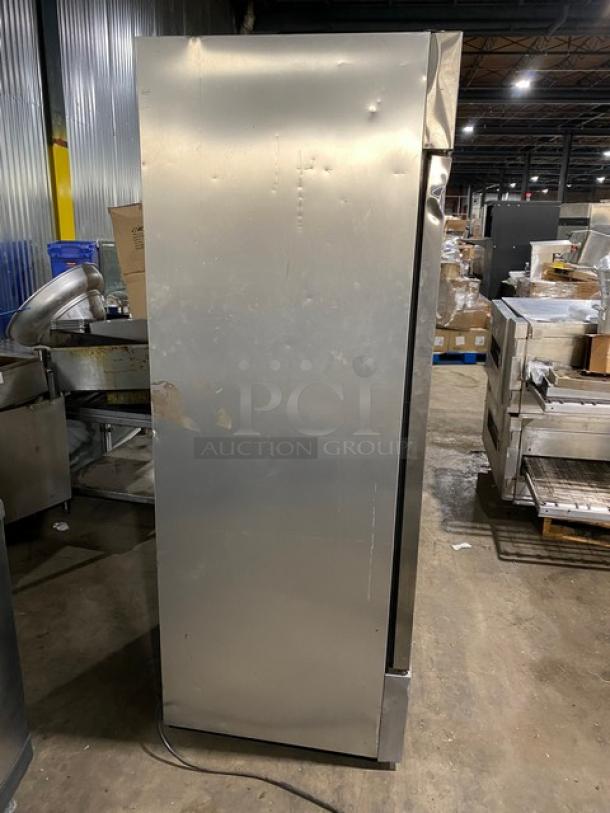 Commercial stainless steel refrigerator, tall and narrow, visible wear and dents, designed for industrial kitchen use.