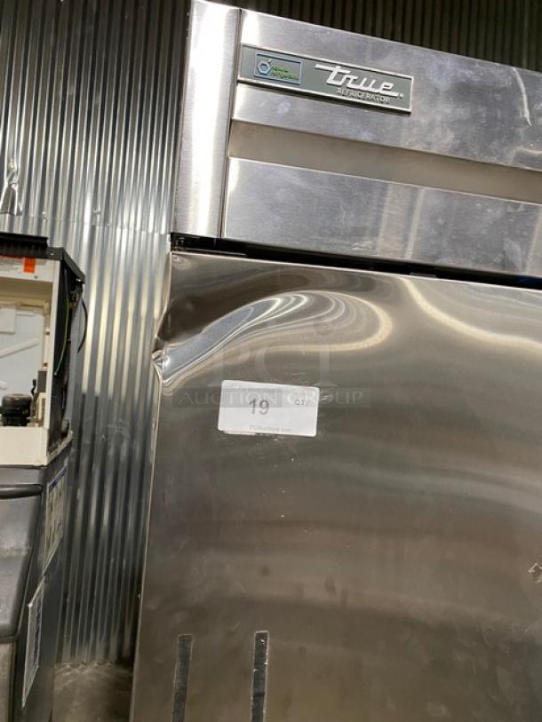 True commercial refrigerator with visible dent on the door; model information and sticker displaying "19 QTY" in auction setting.