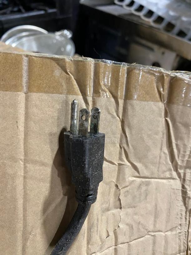 Worn black three-prong electrical cord on a crumpled cardboard surface, showing signs of use and wear.