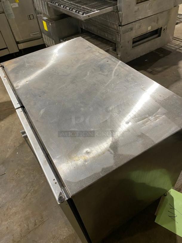 Stainless steel commercial refrigerator, top view, noticeable surface scratches, minor dents, no visible brand or model markings.