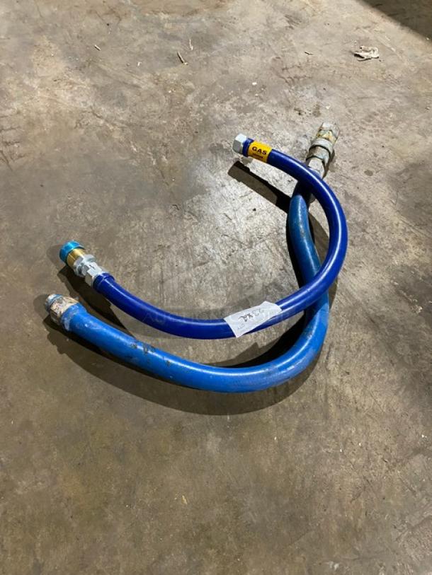 Two blue gas hoses with metal fittings, labeled "GAS" and "24°C," lying on a concrete floor.