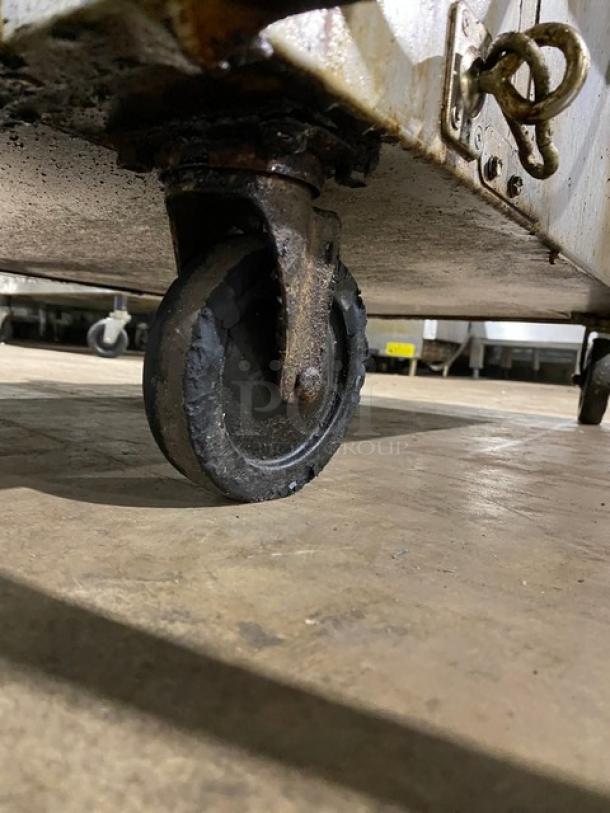 Rusty metal caster wheel attached to the bottom of a metal cart. The wheel shows signs of wear, indicating heavy use.