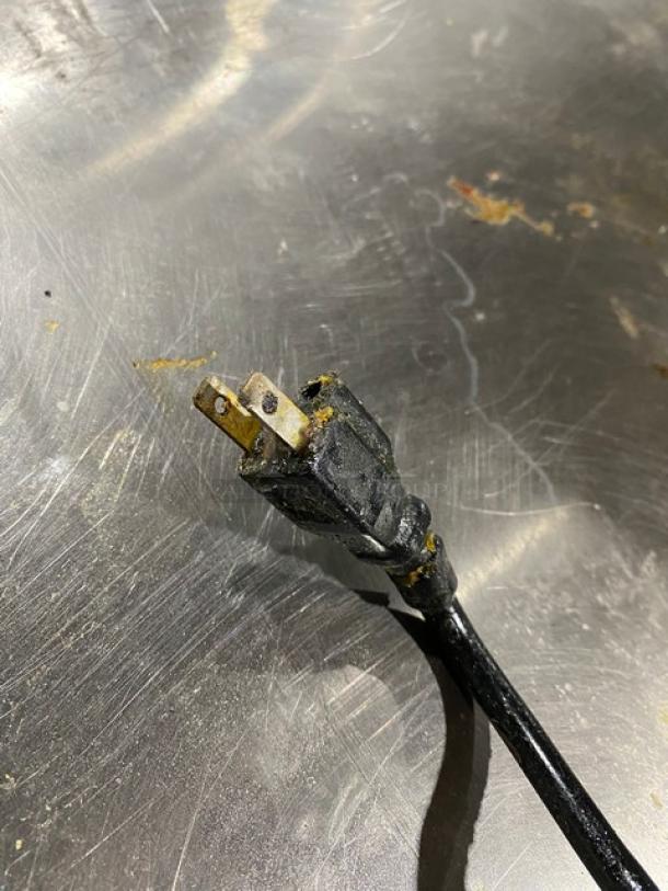 Worn black electrical plug on metallic surface; signs of damage and wear, no visible labels or markings.