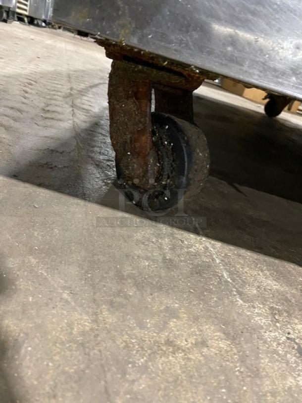 Rusty metal caster wheel on industrial equipment, showing significant wear and corrosion, resting on a concrete floor.