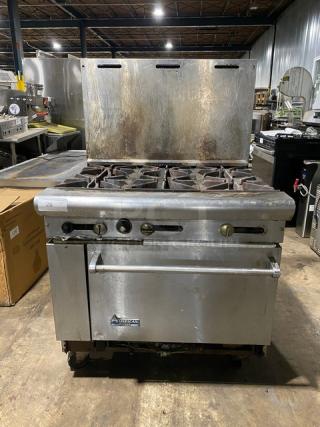 Commercial gas range with six burners, American Range brand. Shows wear from use, ideal for restaurant kitchens.