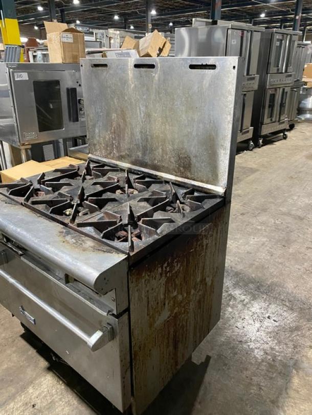 Industrial metal gas stove with six burners and a griddle top. Used condition with visible rust and wear. Ideal for commercial kitchens.