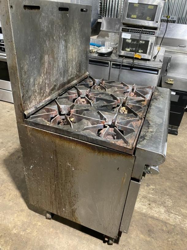 Commercial six-burner gas stove, metal exterior with visible rust and wear, for auction. Ideal for restaurant kitchens.