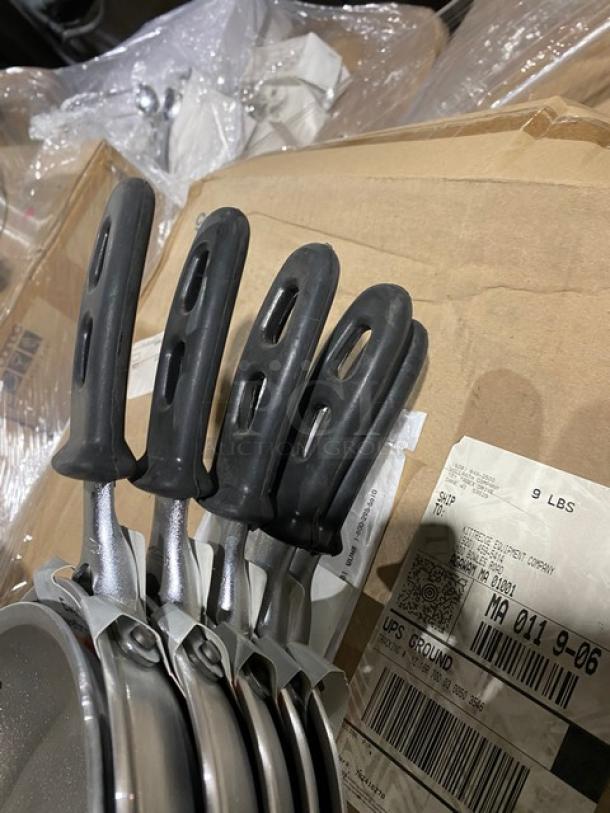 Set of four stainless steel frying pans with black ergonomic handles, new condition. Shipping label visible nearby.