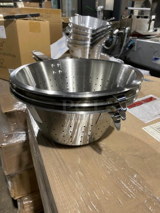 Stack of stainless steel colanders with handles, perforated design, new condition, on a warehouse table.