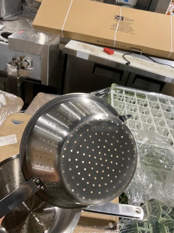 Stainless steel colander with dual handles, perforated design for draining, in new condition. Box markings show model info.