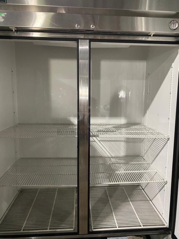 Commercial stainless steel double-door refrigerator, used, with interior wire shelves. Visible thermometer on top right.