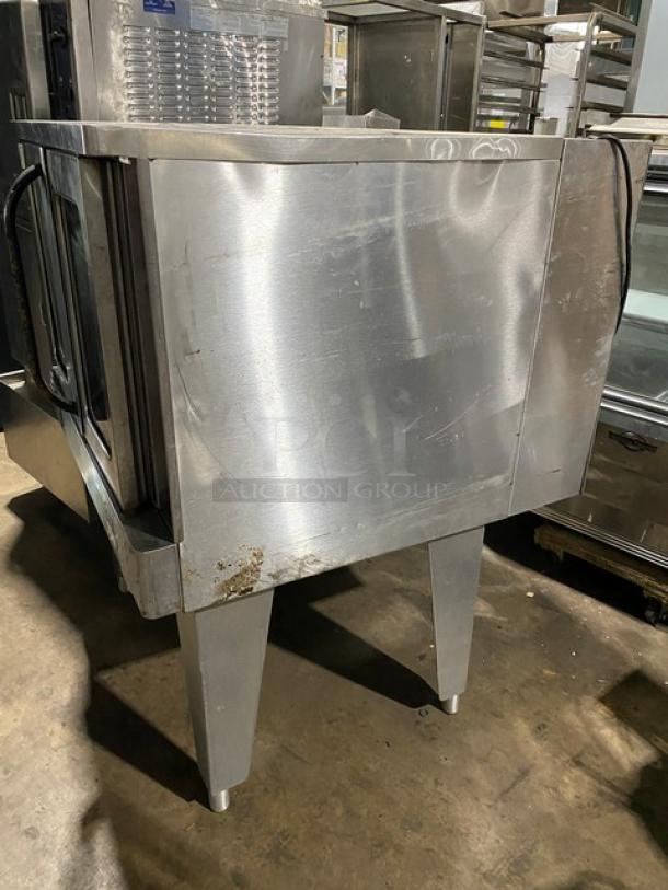 Stainless steel industrial oven with double doors, showing signs of wear and scratches, on four sturdy legs. No visible brand.