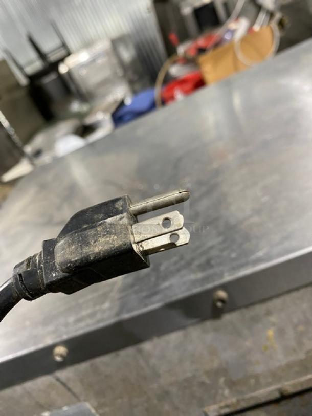 Worn electrical plug with three prongs on a heavy-duty cable, showing signs of wear and dirt, on a metallic surface.