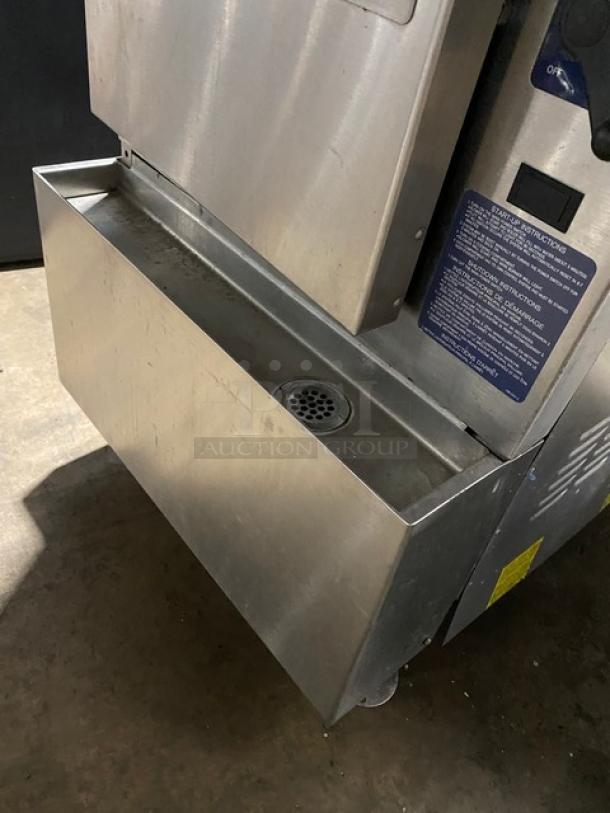 Stainless steel commercial appliance with side drip tray, drain, and instruction label. Industrial design. Good condition.