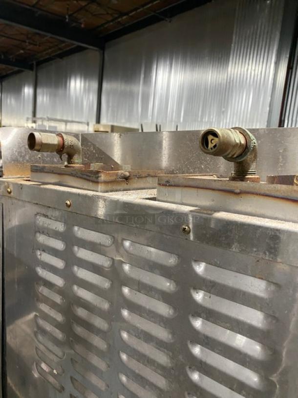 Large industrial metal machine with vents and two pipe fittings. Surface shows wear and rust, highlighting used condition.