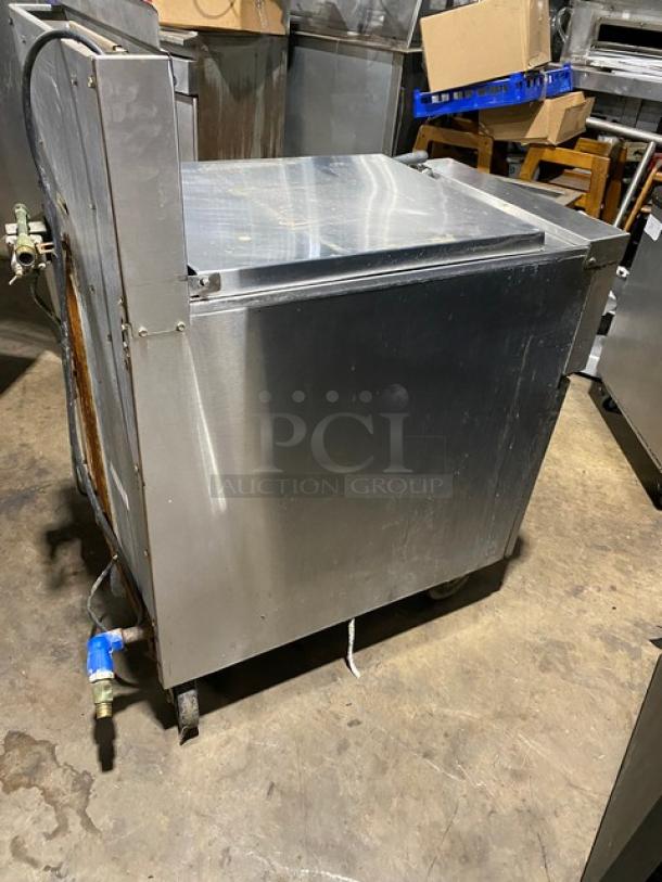 Stainless steel commercial dishwasher, used condition, visible wiring and valve, on wheels for mobility.