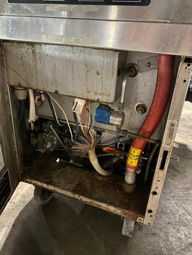 Interior view of a commercial kitchen appliance showing pipes, wires, and a label marked "DRAIN VALVE." Unit has visible rust.