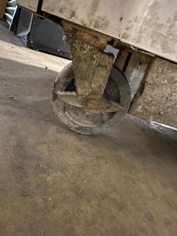 Rusty metal wheel attached to a piece of machinery. Wheel is worn and surrounded by dirt. Rough industrial condition.