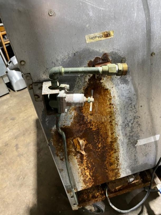 Industrial metal appliance with visible rust and a valve system marked "Hot Water." Aged condition, requires repair.