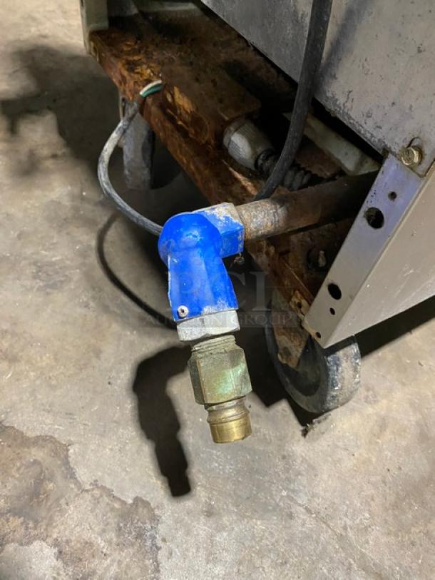Industrial equipment part with blue elbow joint and brass coupling on wheeled metal base, in used condition.